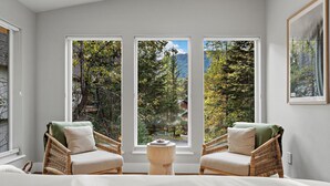 A bedroom with a large window, two wicker chairs, a small wooden stool, and a bed. - Alaska Adventure Retreat LUXURY 4 Bed 5 bath in Girdwood, Base of Alyeska Resort (Anchorage)