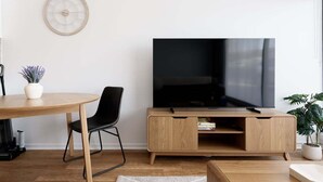 A modern living room with a wooden TV stand, a round dining table, a black chair, and a potted plant. - Minimalist Studio Near Burnie | Clean & Cozy (Hillcrest)