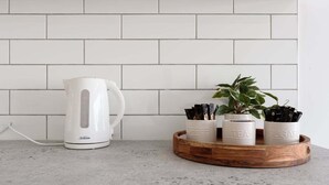 A kitchen with a white kettle, a tray with labeled containers for coffee, tea, and sugar, and a potted plant. - Minimalist Studio Near Burnie | Clean & Cozy (Hillcrest)