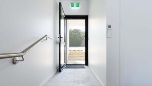 A stairway with a handrail, a door with an emergency exit sign, and a control panel on the wall. - Minimalist Studio Near Burnie | Clean & Cozy (Hillcrest)