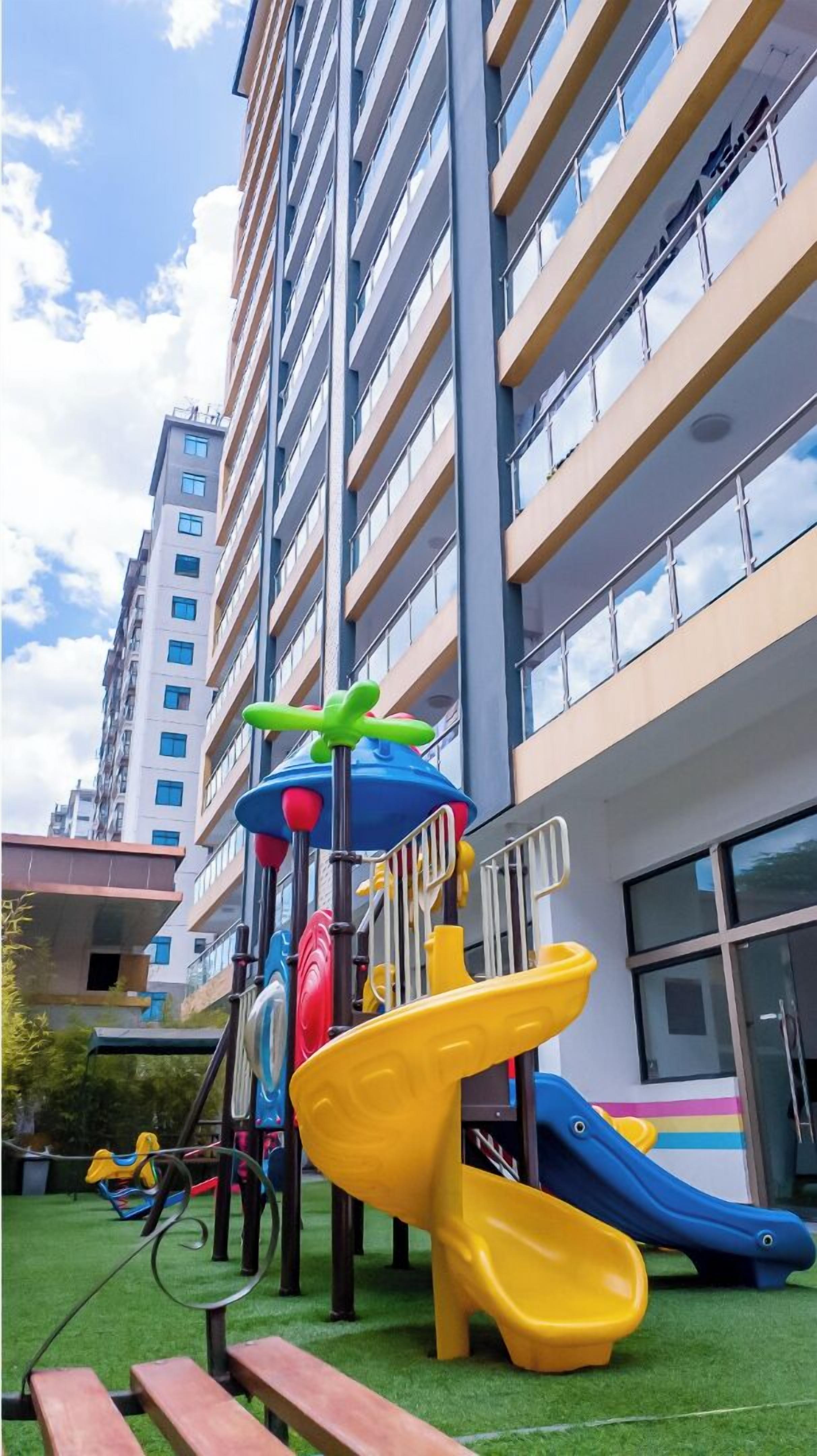 A playground with slides and climbing structures in front of a tall residential building.