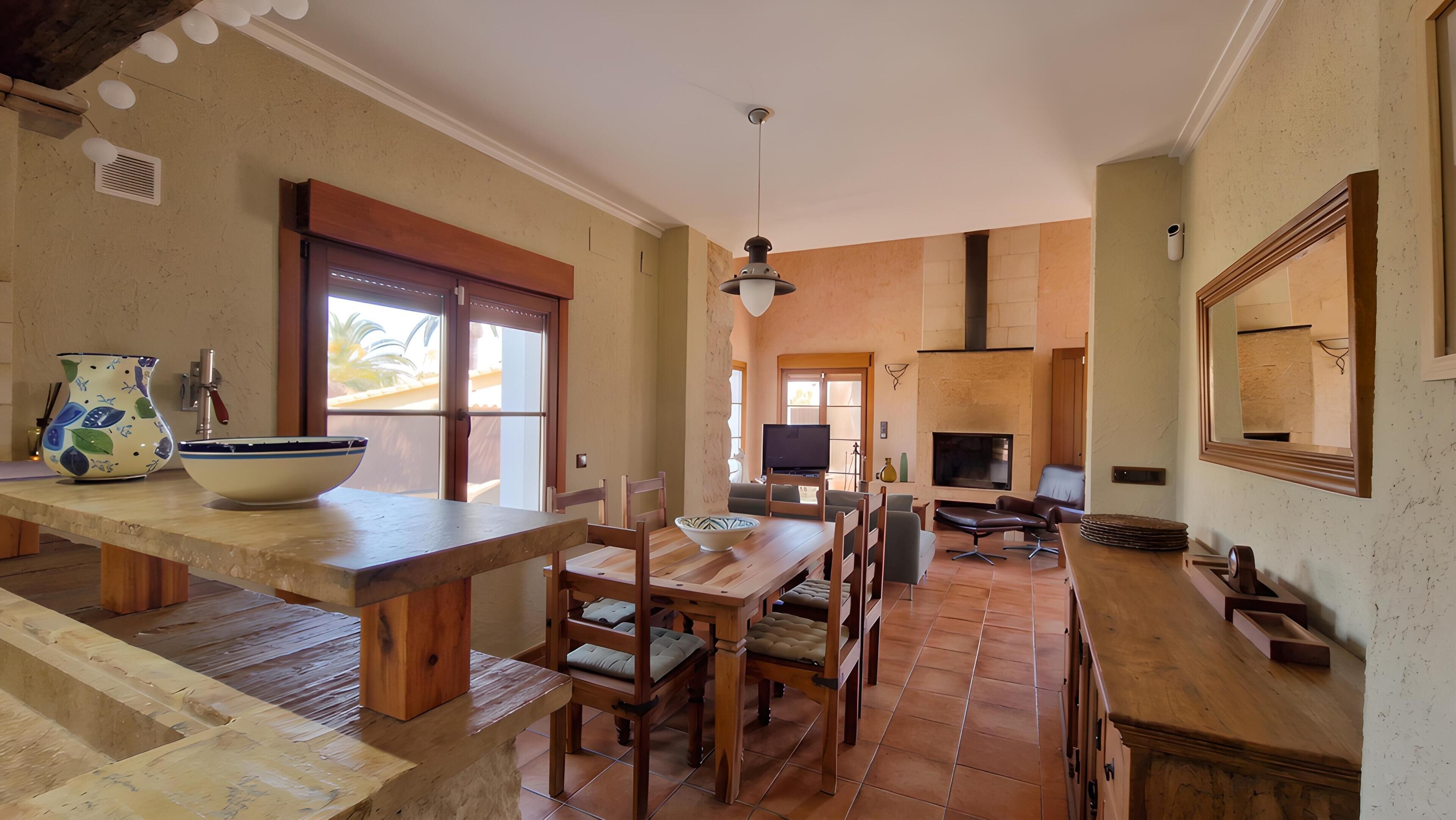 A spacious kitchen with a dining area, wooden furniture, a large window, and a fireplace.