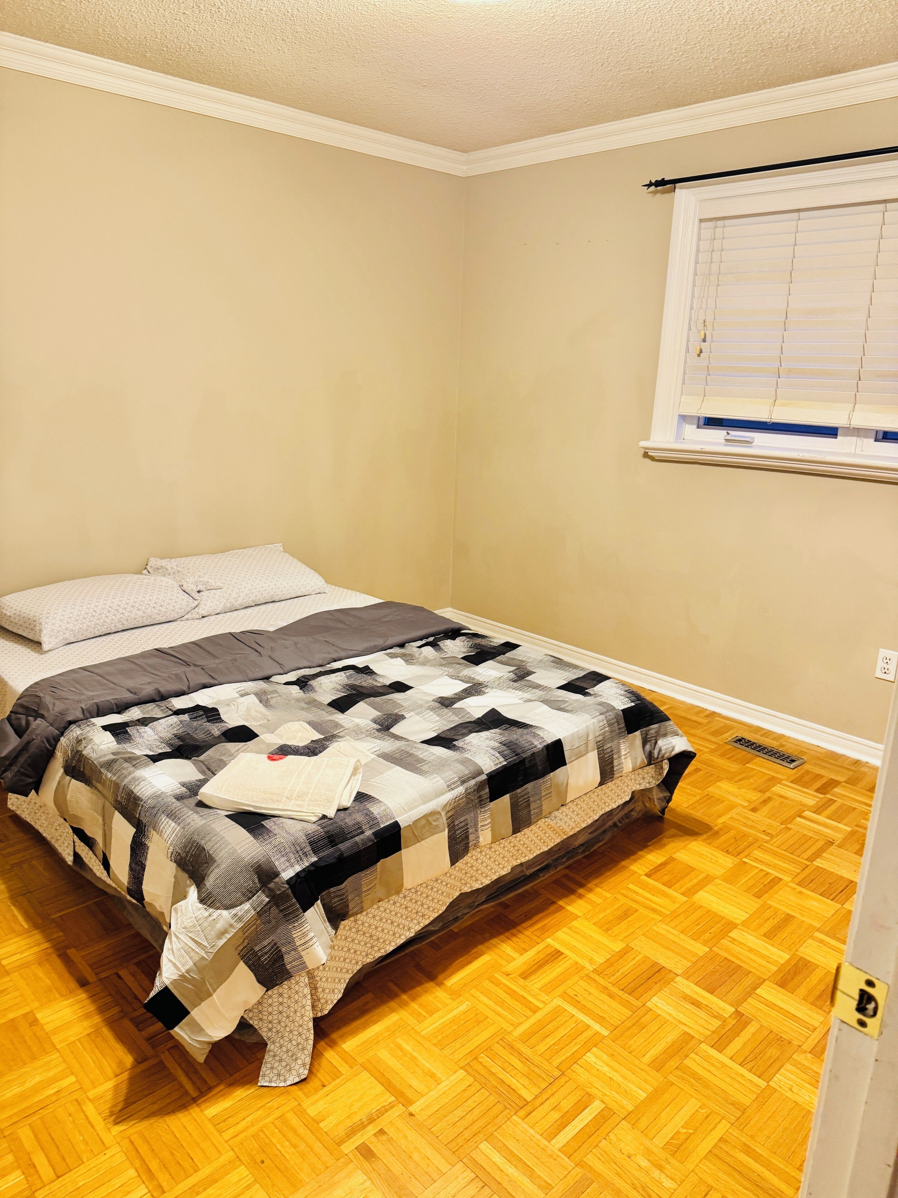 A bedroom with a bed, a window with blinds, and a wooden floor.