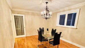 A dining room with a glass table and chairs, a chandelier, wooden flooring, a door with a glass panel, and a window with blinds. - Luxury House 10 Bdrms - Near Airport, sq 1, Private Backyard (Mississauga)