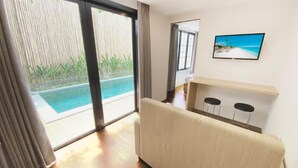 A room with a sofa, a TV, a small bar area, and a view of a pool. - Pamela Bali (Keroboken Kelod)
