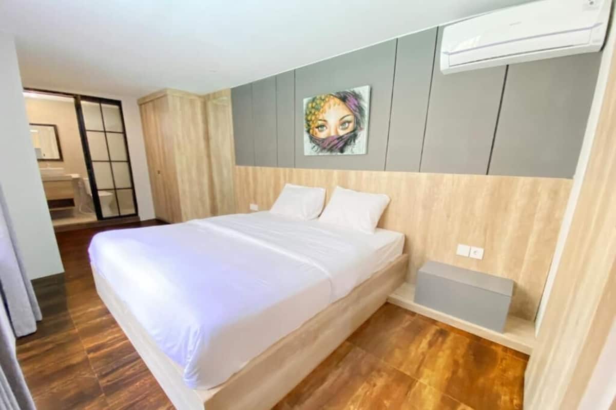 Una camera da letto con un letto, pavimento in legno, condizionatore d'aria a parete e un piccolo comodino.