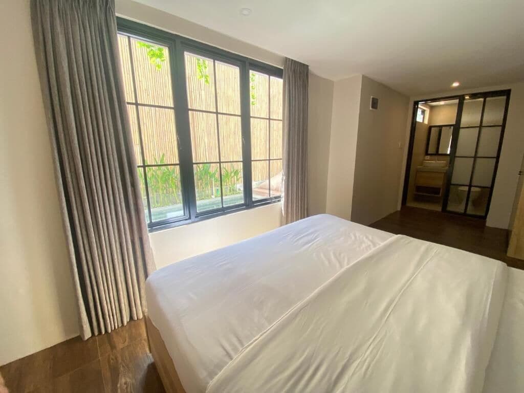 Habitación de hotel con una cama, una ventana con cortinas y vistas a la vegetación.