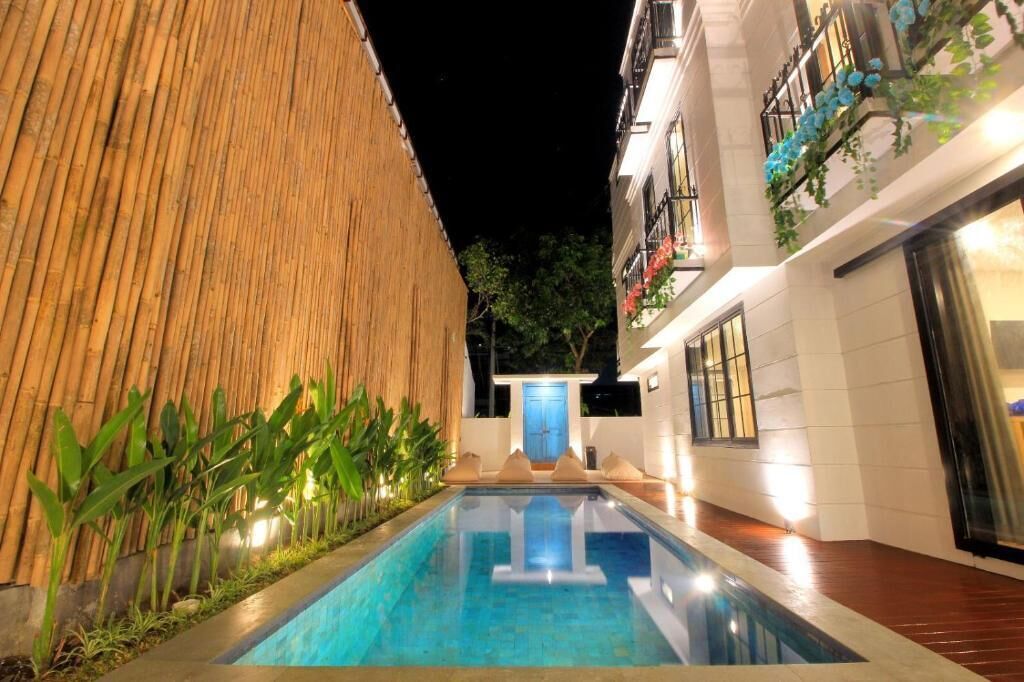 A pool area with a bamboo wall, a blue door, and a building with balconies.