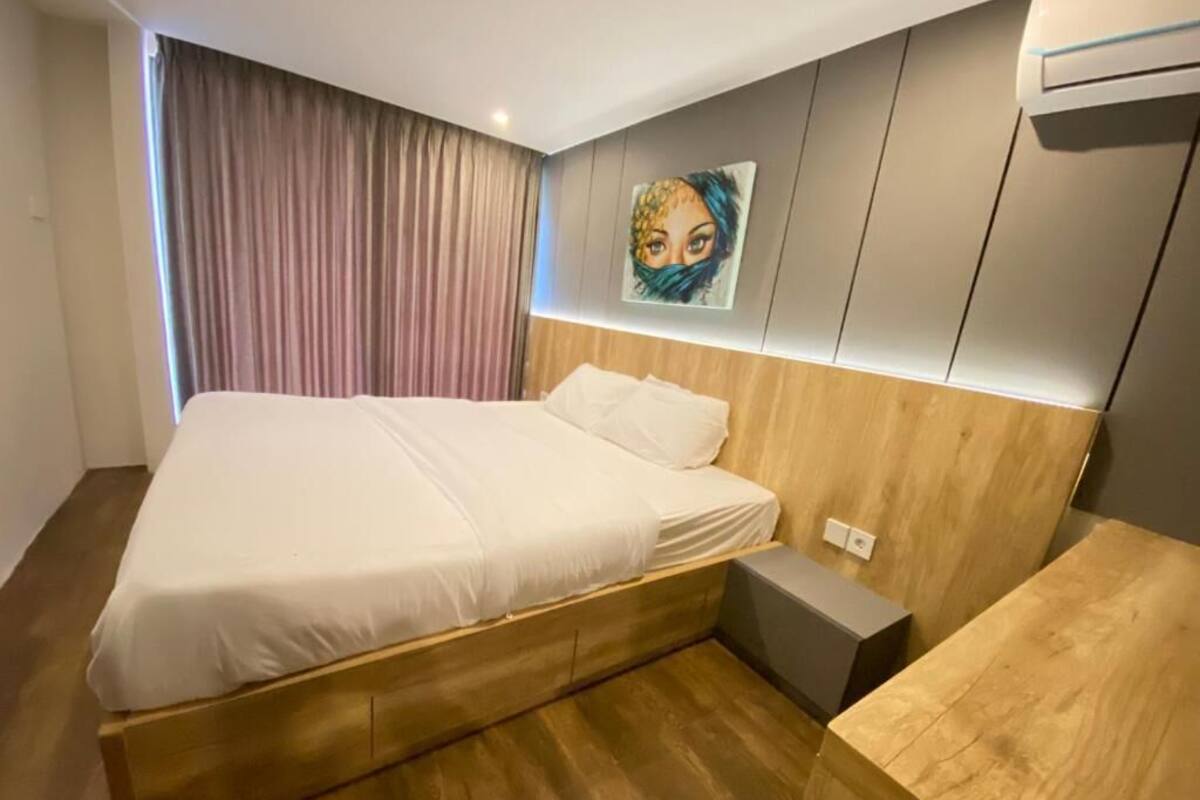 Una camera da letto con un letto di legno, un comodino, un condizionatore d'aria a parete e un'ampia finestra con tende.