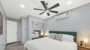 A hotel room with a bed, a ceiling fan, an air conditioning unit, a bedside table with a lamp, and a mirror. - Broadway Casita - Remodeled Minutes from U of A (Tucson)