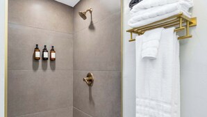A bathroom with a shower, a towel rack with towels, and three bottles of soap. - Broadway Casita - Remodeled Minutes from U of A (Tucson)