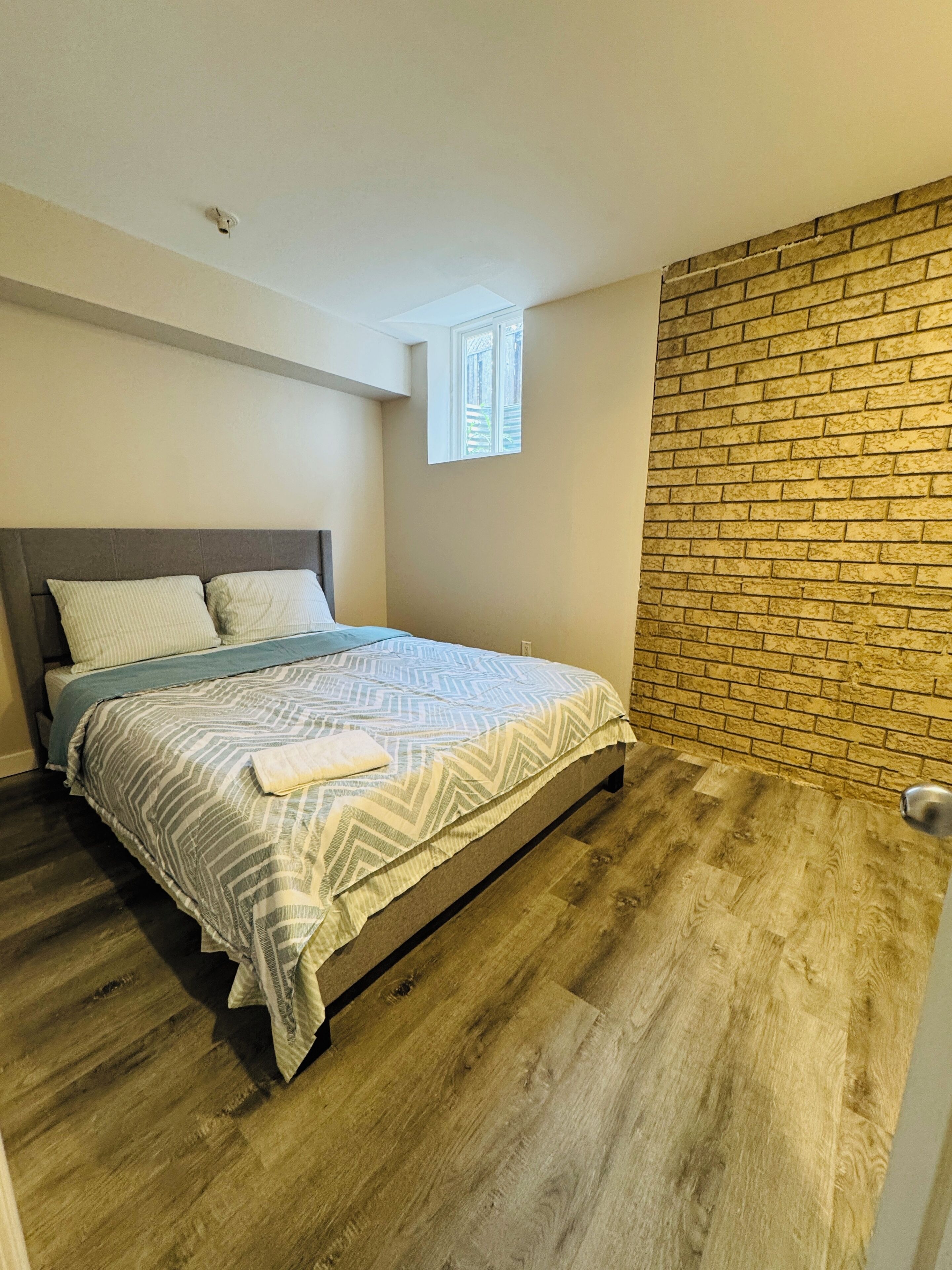 Un dormitorio con cama, ventana, pared de ladrillo y puerta.