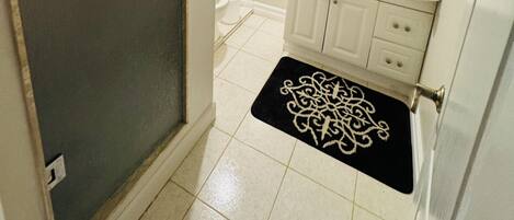 A bathroom with a white sink, a mirror with a gold frame, a towel rack, and a black and white rug.