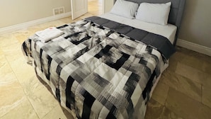 Una camera da letto con un letto, una testiera grigia e una coperta a quadri.