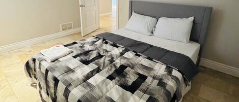 A bedroom with a bed, a gray headboard, and a checkered bedspread.
