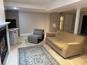 A living room with a beige sofa, a gray armchair, a small refrigerator, a TV, and a patterned rug. - 3 Bdrms - Near Airport, sq 1 (Mississauga)