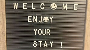 A welcome sign with the text 'WELCOME ENJOY YOUR STAY!' on a black background with horizontal lines. - Room-haven in the Prairies Full 2BR (Winnipeg)