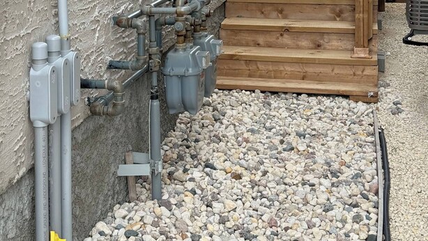 A utility area with pipes, a water meter, and a wooden deck. - Room-haven in the Prairies Full 2BR (Winnipeg)