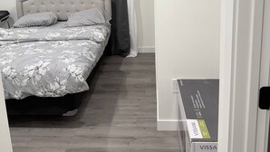 A bedroom with a bed, grey curtains, a white wall, and a wooden floor. - Room-haven in the Prairies Full 2BR (Winnipeg)