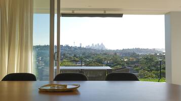 A dining area with a table and chairs, a view of a cityscape through a balcony, and a large window with curtains.