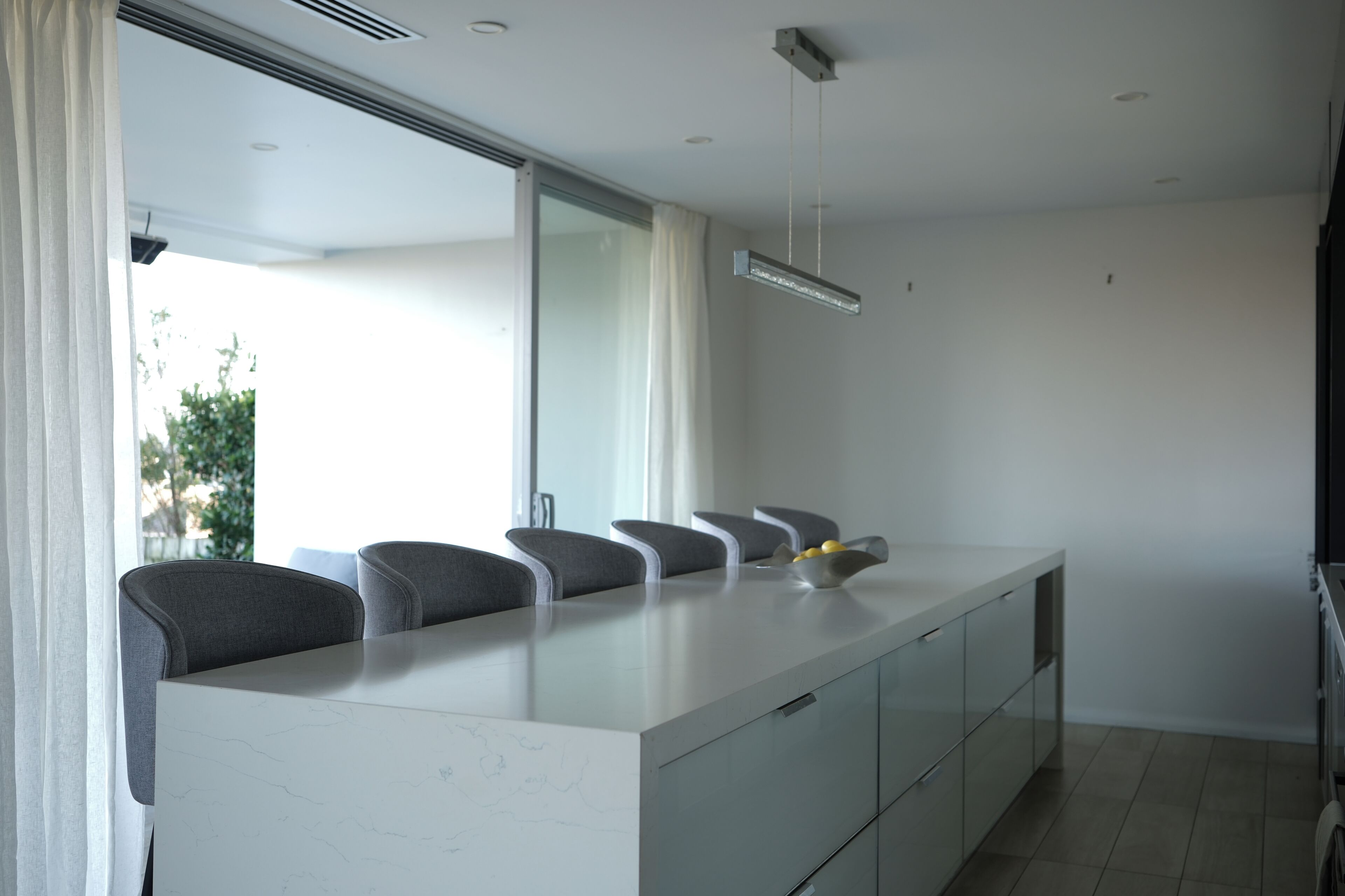 A modern kitchen with a marble countertop, grey chairs, and a large window.
