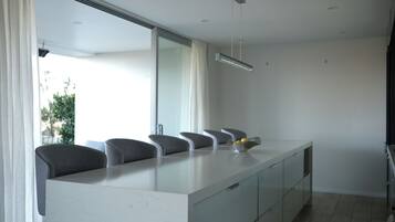 A modern kitchen with a marble countertop, grey chairs, and a large window.