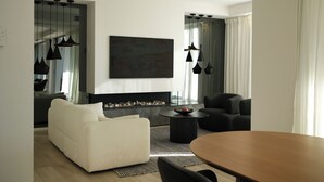 Una sala de estar moderna con chimenea, un sofá blanco, un sillón negro, una mesa de comedor y lámparas colgantes.