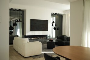 Ein modernes Wohnzimmer mit Kamin, einem weißen Sofa, einem schwarzen Sessel, einem Esstisch und Pendelleuchten.
