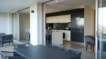 A modern kitchen with dark cabinets and a central island, a dining area with a dark table and chairs, and a view through a glass door.