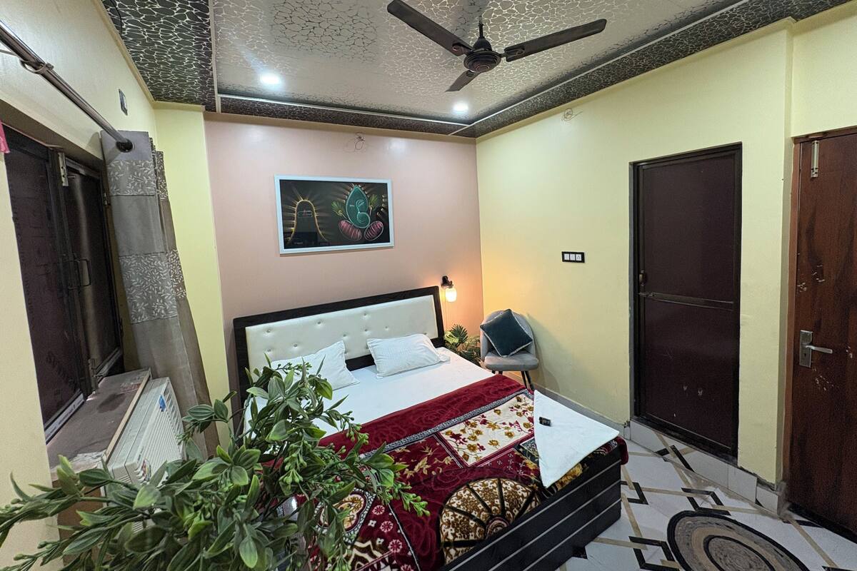 A bedroom with a bed, a ceiling fan, a wall-mounted light, a door, and a radiator.