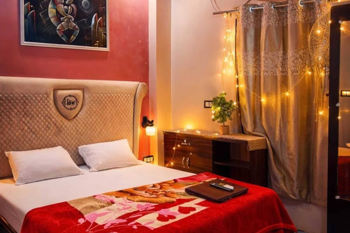 A hotel room with a bed, a desk, an air conditioner, and a painting on the wall.