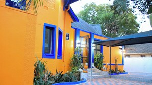 A building with a bright orange exterior, blue-framed windows, and a covered entrance area with steps. - Neo & Ruks Guest House Parow (Cape Town)