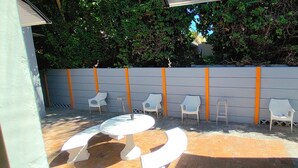 An outdoor patio with a round table and chairs, a white wall with orange accents, and a brick floor. - Neo & Ruks Guest House Parow (Cape Town)