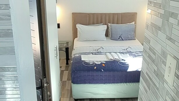 A bedroom with a bed, a nightstand, a lamp, and a window with bars. - Neo & Ruks Guest House Parow (Cape Town)