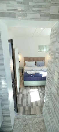A bedroom with a bed, a nightstand, a lamp, and a window with bars.