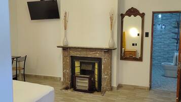 A room with a fireplace, a television mounted on the wall, a mirror, and a bathroom visible through an open door.