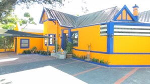 A colorful building with a blue and yellow facade, a tiled roof, and a paved entrance area with potted plants. - Neo & Ruks Guest House Parow (Cape Town)