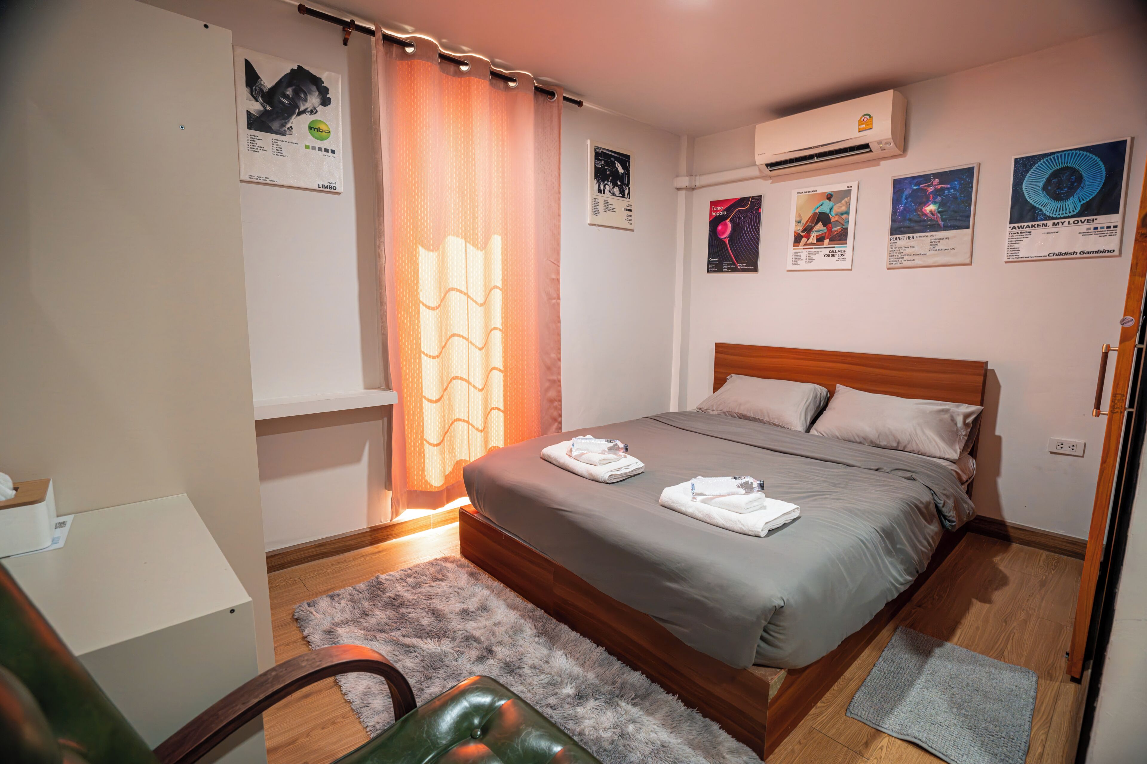 A bedroom with a bed, a desk, a chair, an air conditioner, and wall art.