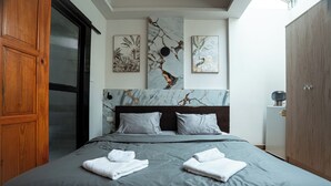 Una cama bien hecha con ropa de cama gris, un armario de madera y tres obras de arte colgadas en la pared.