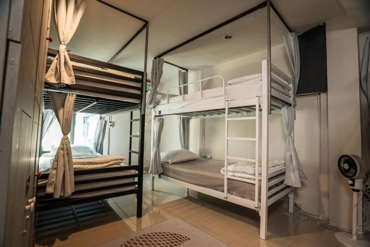 A bunk room with a bunk bed, a desk, a chair, and a fan.
