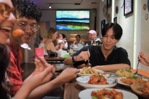Eine Gruppe von Personen isst in einem Restaurant, im Hintergrund läuft ein Fernseher.