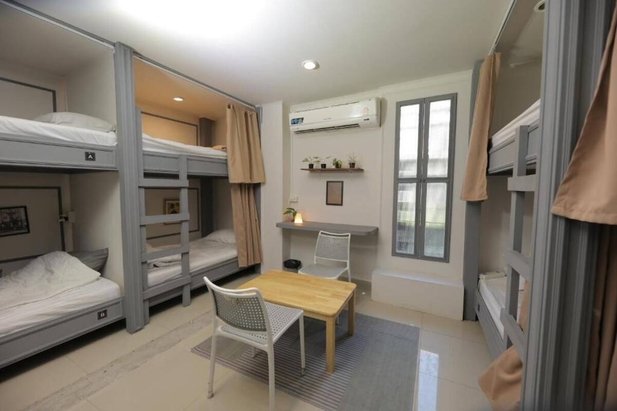 A dorm-style room with bunk beds, a desk, chairs, and an air conditioning unit.
