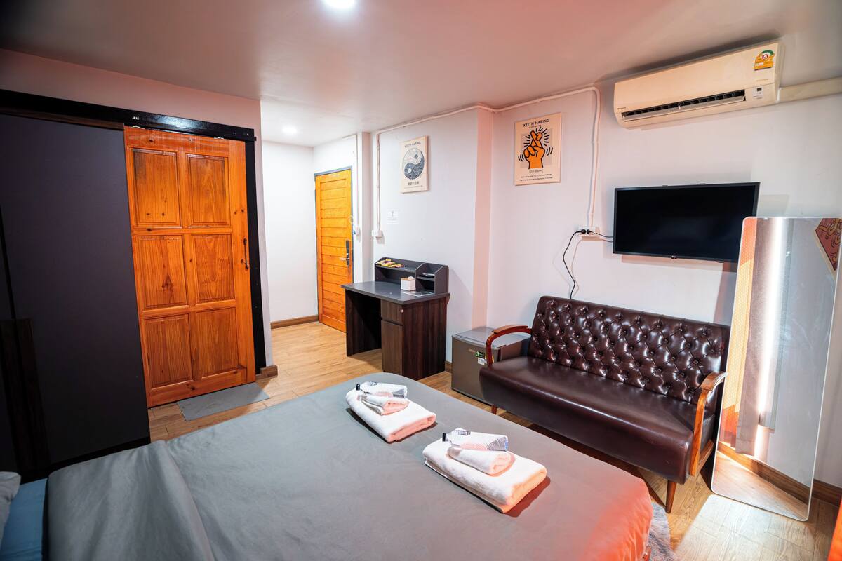 A hotel room with a bed, a sofa, a TV, a wardrobe, and a desk.
