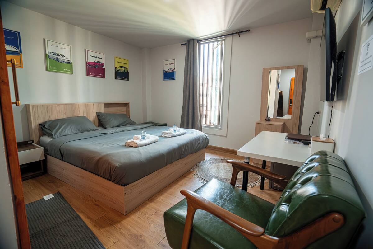 A bedroom with a bed, a desk, a chair, a mirror, and wall art.