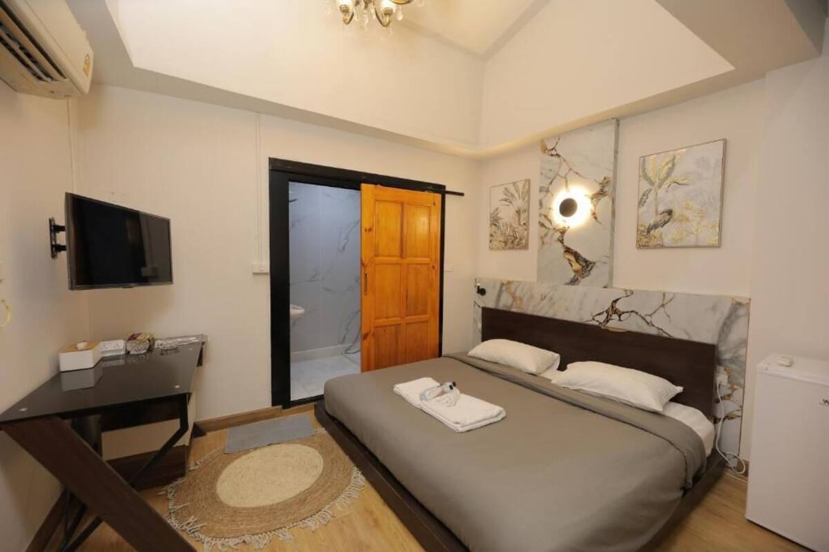 A bedroom with a bed, a desk, a television, a door, and artwork on the walls.