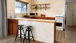 A modern kitchen with a central island, bar stools, a microwave, a stove, and a window with a view. - Cosy 3BR Cottage Home w/ Ample Parking (Slacks Creek)