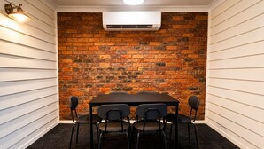 A conference room with a brick wall, white paneling, a table, and four chairs. - Cosy 3BR Cottage Home w/ Ample Parking (Slacks Creek)
