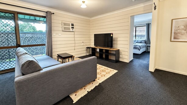 A modern living room with a sofa, TV, and ceiling fan. - Cosy 3BR Cottage Home w/ Ample Parking (Slacks Creek)