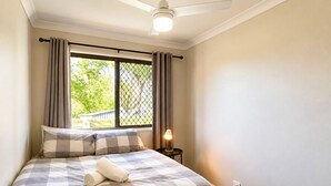 A bedroom with a bed, a ceiling fan, a window with curtains, and a nightstand with a lamp. - Cosy 3BR Cottage Home w/ Ample Parking (Slacks Creek)