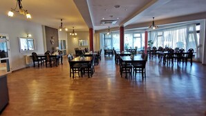 A spacious dining area with multiple tables and chairs, large windows, and ceiling lights. - Hotel Zieliniec (Poznań)